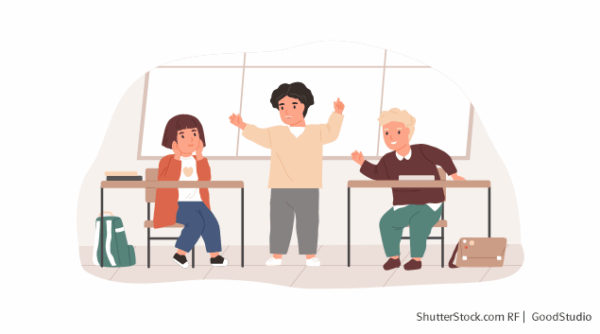 Drei Kinder im Klassenzimmer, zwei Kinder sitzen an Schreibtischen und ein Kind steht in der Mitte mit den Armen in der Luft