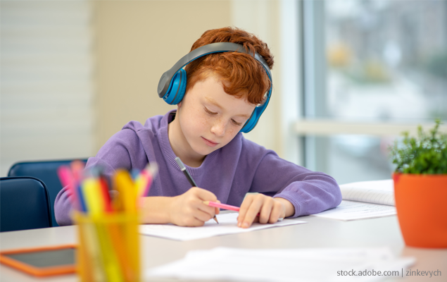 Grundschul-Blog-Unterrichten-Diagnostik_Kind_mit_Kopfhörern Kind hat Kopfhörer auf und schreibt auf einem Blatt Papier