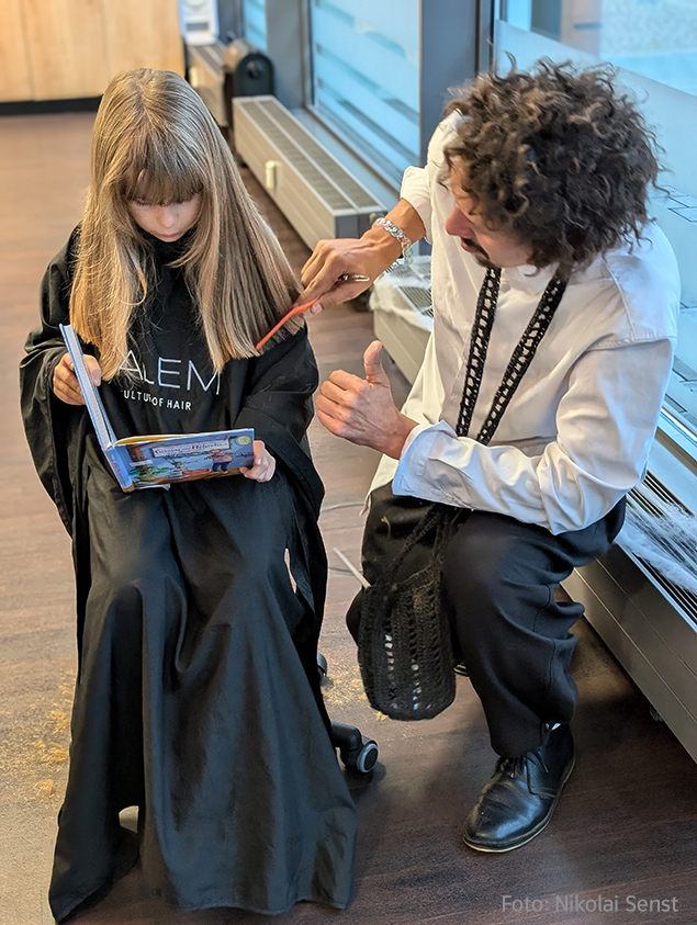 Grundschul-Blog-Vorlesetag-Vorlesefriseur-Danny-Beuerbach Foto Vorlesefriseur Danny Beuerbach mit Mädchen, das vorliest beim Haareschneiden